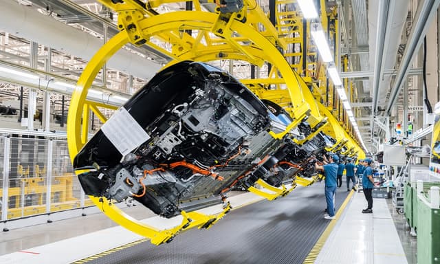 Car assembly line with yellow robotic rings — precision manufacturing